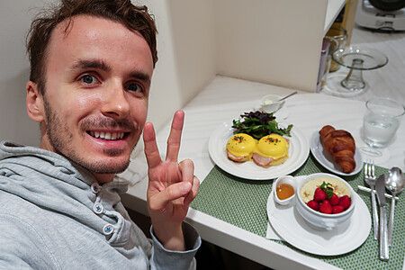 Marco Togni sorride facendo il segno di vittoria davanti a un tavolo con uova alla benedettina e frutta presso Sarabeth.