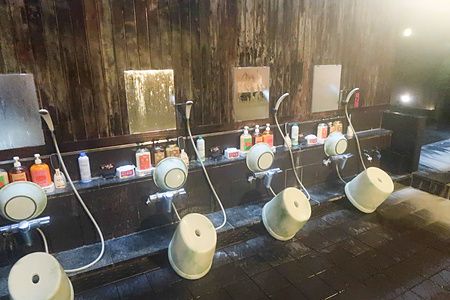 Area docce dell'onsen a Oku Nikko Hotel Shikisai con docce a mano e sgabelli.