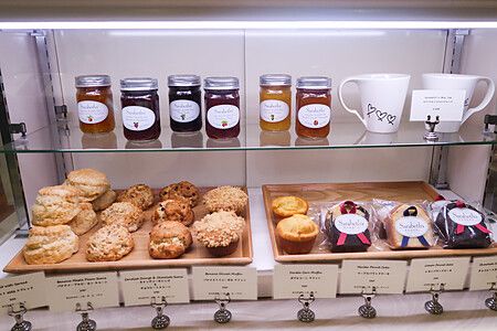 Vetrina di un ristorante Sarabeth a Tokyo con vasetti di confettura, tazze bianche, muffin e scone su vassoi di legno.
