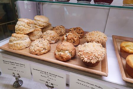 Una teca di vetro contiene vassoi di legno con diversi Scone e un Muffin nel ristorante Sarabeth a Tokyo.