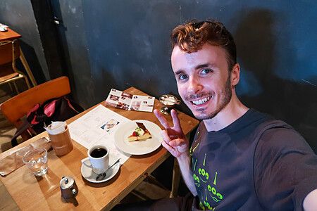 Marco Togni che sorride con caffè e torta al Sarasvati, Miyajima.