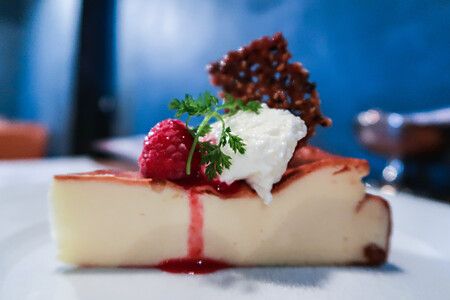 Fetta di torta con lampone e panna su piatto bianco.