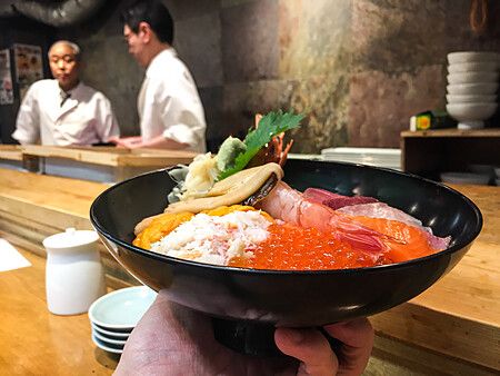 Una ciotola di kaisendon con pesce fresco tenuta in mano davanti al bancone del ristorante Tsukiji Itadori Bekkan.