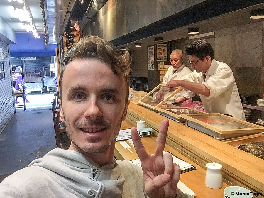 Marco Togni sorridente al ristorante Tsukiji Itadori Bekkan con chef al lavoro.