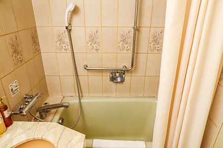 Un bagno compatto all'hotel Dormy Inn in Giappone con vasca verde, piastrelle beige a motivi floreali e doccino.