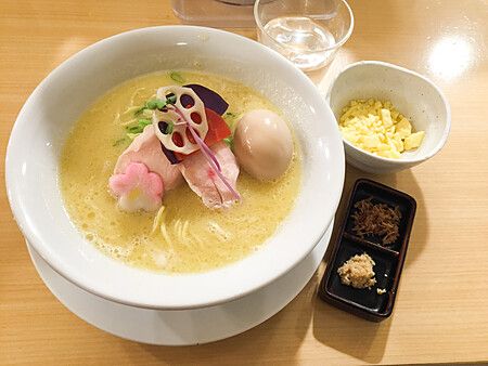 Una ciotola di ramen con brodo giallo, pollo e guarnizioni su un tavolo di legno al ristorante Kagari Ramen a Tokyo.