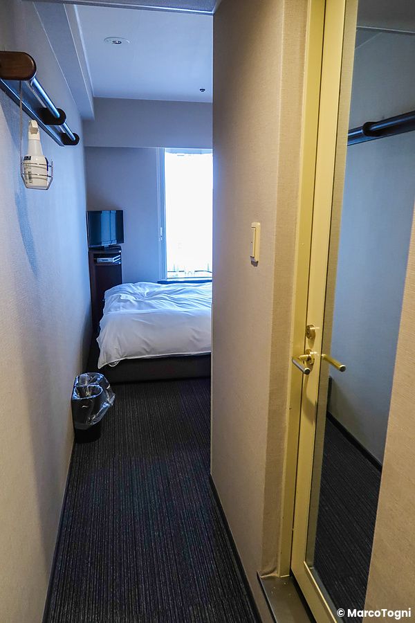 Interno di una camera d'albergo all'hotel Dormy Inn con corridoio d'ingresso, letto e televisore vicino alla finestra.