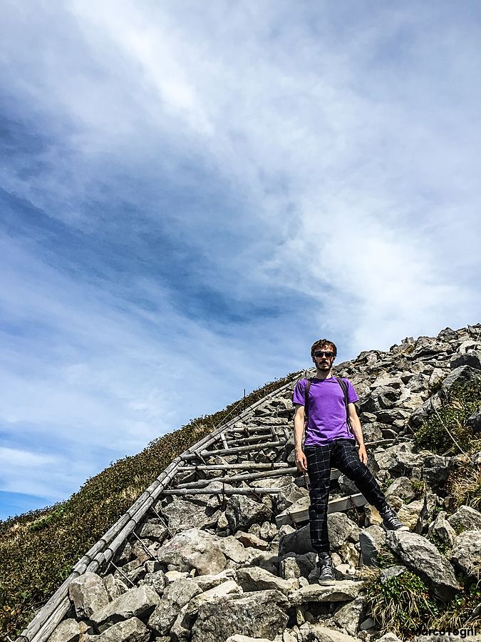 Persona su sentiero roccioso del monte Iwaki sotto cielo limpido.