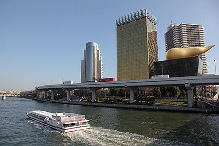 Un battello naviga sul fiume Sumida di fronte all'Asahi Beer Hall con la sua tipica scultura dorata a Tokyo.