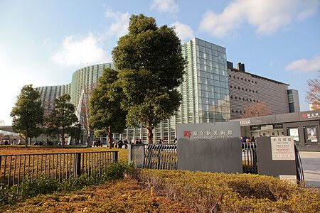 Facciata di vetro di The National Art Center a Tokyo con alberi e cielo blu.