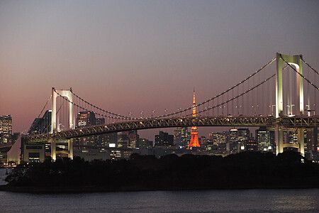 Veduta notturna del Rainbow Bridge a Tokyo con la Tokyo Tower visibile sullo sfondo illuminato della città.