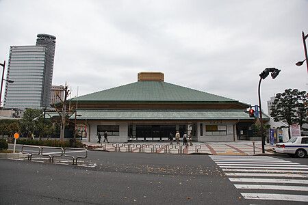 L'esterno del Ryogoku Kokugikan a Tokyo con il suo caratteristico tetto verde e persone che camminano verso lo stadio.