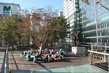 Terrazza a Shiodome, Tokyo, con sculture di mucche colorate e un albero.