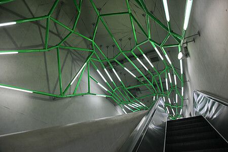 Scala mobile nella stazione di Iidabashi a Tokyo con tubi verdi e luci al neon.