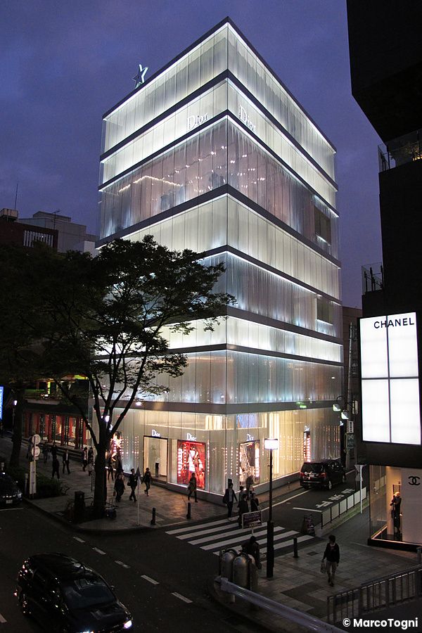 Edificio di lusso illuminato a Omotesando, Tokyo, con persone sul marciapiede.