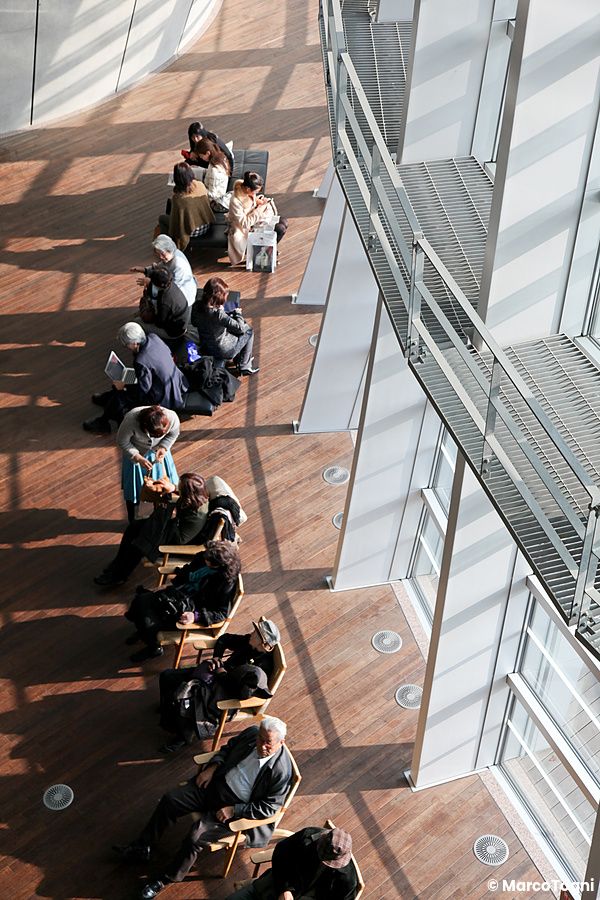 Persone sedute lungo un corridoio luminoso al The National Art Center, Tokyo.