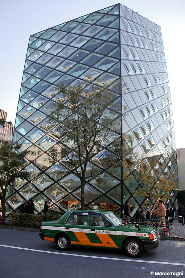 Edificio Prada Aoyama a Tokyo, architettura in vetro con taxi davanti.