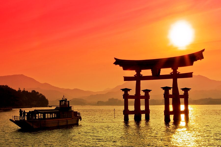 Torii Gate al tramonto con barca sullo sfondo a Miyajima, Giappone.