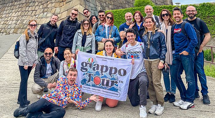 Un gruppo di viaggiatori con la bandiera con logo GiappoTour, e Marco Togni a terra, davanti alle mura del castello di Osaka.