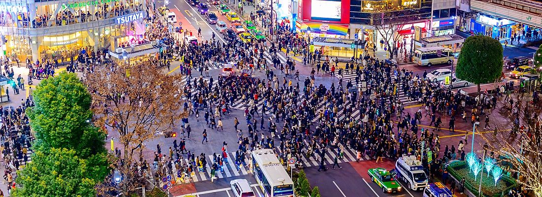 Folla attraversa Shibuya Crossing a Tokyo di notte con luci al neon.