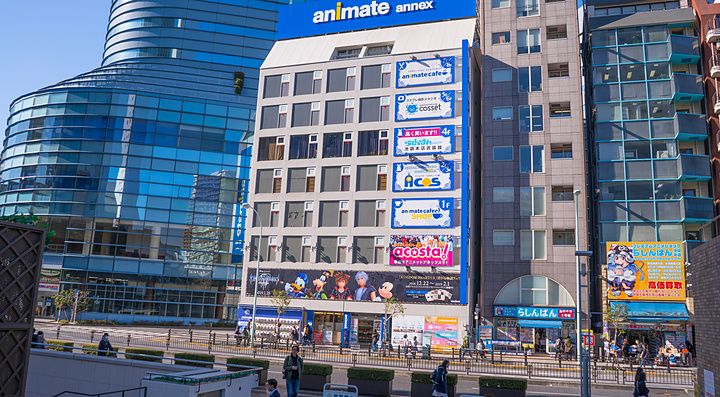 Edificio Animate Annex a Ikebukuro con insegne colorate e passanti che camminano sul marciapiede in un giorno di sole.