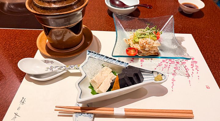 Antipasti a Ume no Hana a Ginza serviti in raffinati piatti di ceramica e vetro su una tovaglietta illustrata.