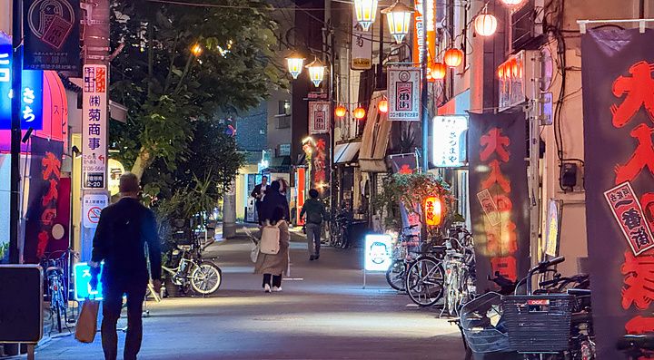 Veduta notturna di una strada nel quartiere di Asagaya a Tokyo con lanterne e persone che camminano tra le biciclette.