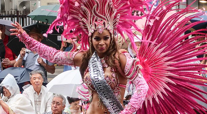 Una ballerina in costume da samba rosa con piume sfila all'Asakusa Samba Carnival sotto la pioggia tra la folla.