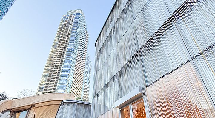 Boutique di lusso con facciata a fili metallici presso Azabudai Hills a Tokyo, con grattacieli sullo sfondo.