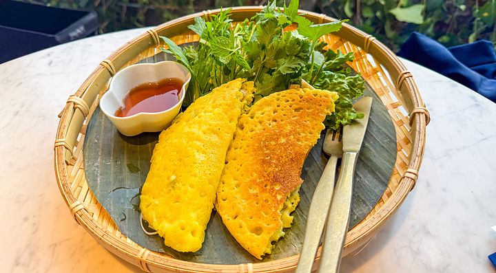 Un piatto di bánh xèo, crêpe vegana, servito su una foglia di banano in un vassoio di vimini al Lotus Palace di Fukuoka.