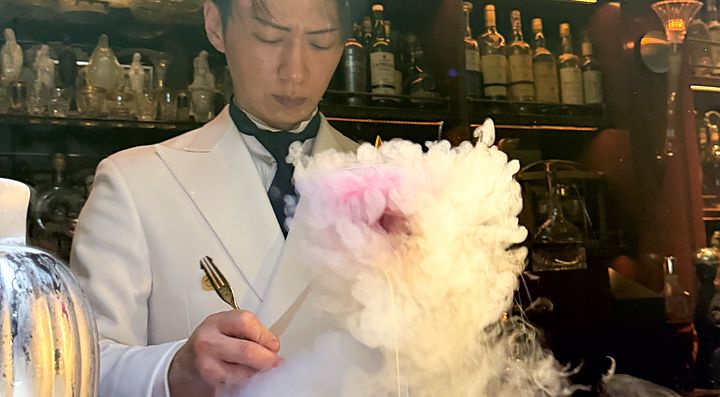 Un barista in divisa bianca prepara un cocktail fumante dietro il bancone del Bar Centifolia a Tokyo.