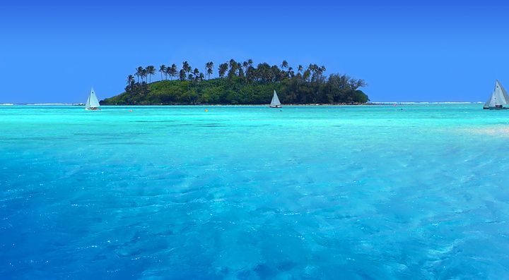 Barche a vela vicino a un'isola tropicale con acque turchesi.