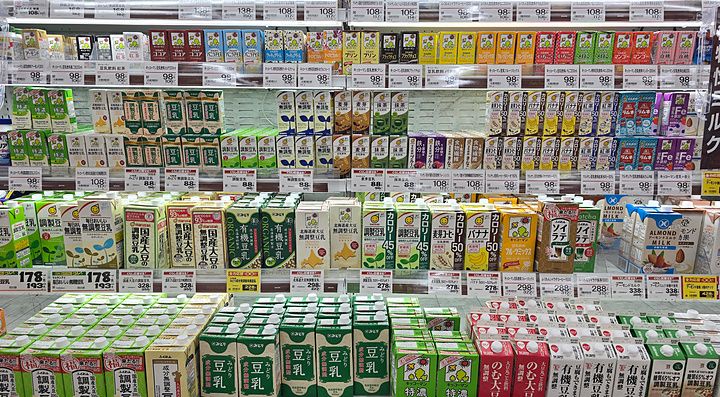 Scaffali refrigerati pieni di vari cartoni di latte vegetale in un supermercato in Giappone.