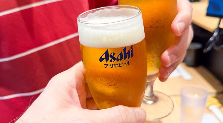 Due persone brindano con bicchieri di birra Asahi all'interno del ristorante Sushi Uogashinihonichi.