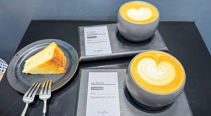 Due tazze di caffè con latte art e una fetta di dolce su un tavolo nero presso X coffee a Ginza, Tokyo.
