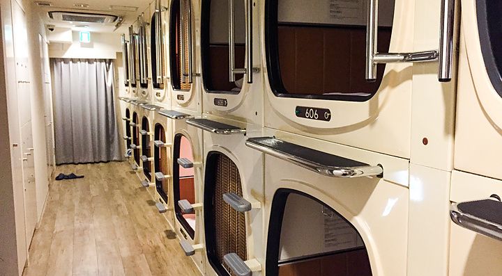 Corridoio di un hotel capsule a Tokyo con una fila di moduli letto impilati su due livelli.