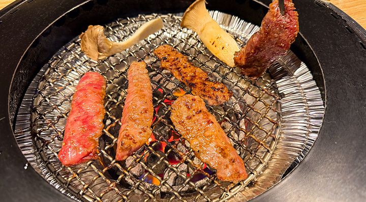 Tagli di carne e funghi che cuociono su una griglia circolare all'interno del Ristorante Toraji.