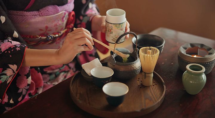 Una persona in kimono versa polvere di matcha in una teiera durante una cerimonia del tè tradizionale.