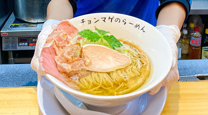La chef a Ramen Chonmage Osaka Tenroku Ten sorride tenendo una ciotola di ramen preparata nel ristorante.