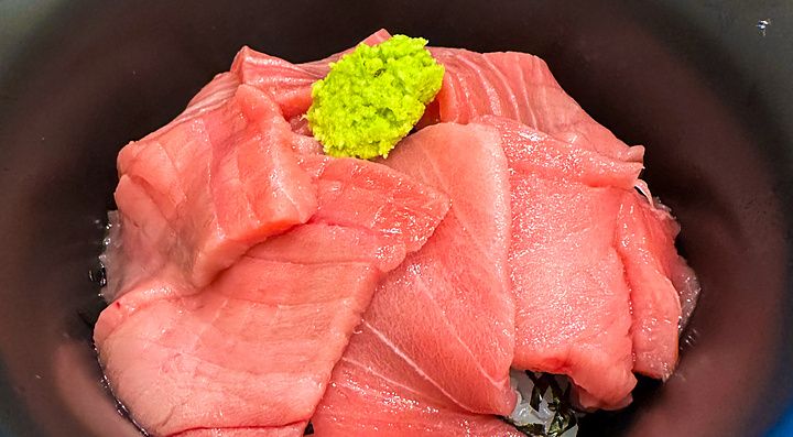Una ciotola nera contenente fette di tonno crudo e wasabi su una base di riso servita presso Maguro Koya a Nara.