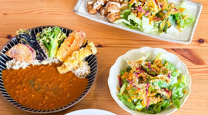 Piatti di curry, insalata, falafel e molto altro a Marugoto, ristorante vegano ad Asakusa, su un tavolo di legno.