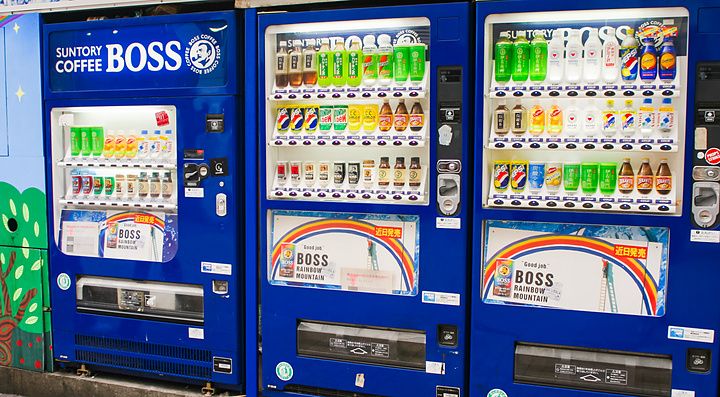 Tre distributori automatici di bevande Suntory Boss blu allineati su una strada in Giappone.
