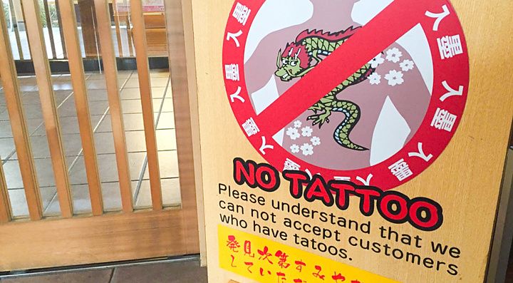Un cartello informativo su un cavalletto in legno che comunica il divieto di tatuaggi in un onsen.