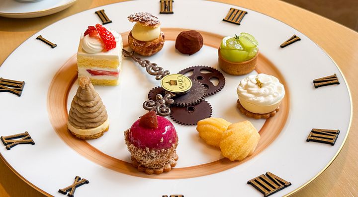 Una selezione di dolci su piatto a forma di orologio a Wako Tea Salon con numeri romani e lancette decorative.
