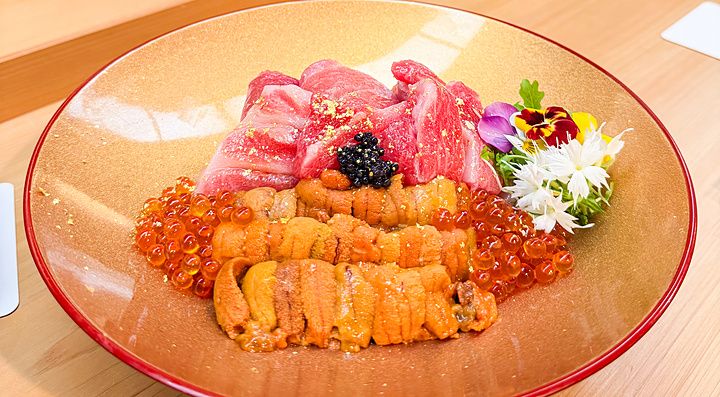 Un donburi premium con ikura, riccio di mare, chutoro e otoro servito su un piatto dorato presso il ristorante Waunn.