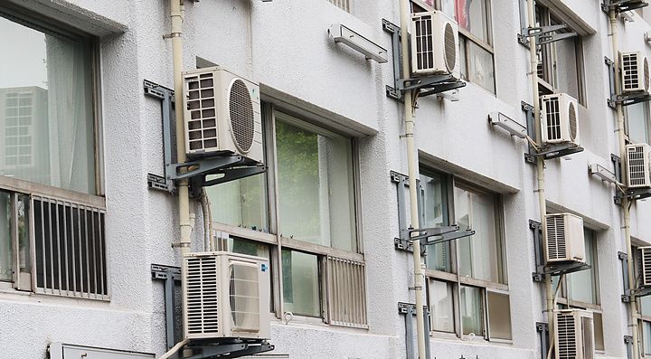 Facciata di un edificio residenziale a Tokyo con numerose unità esterne di condizionatori installate in serie.