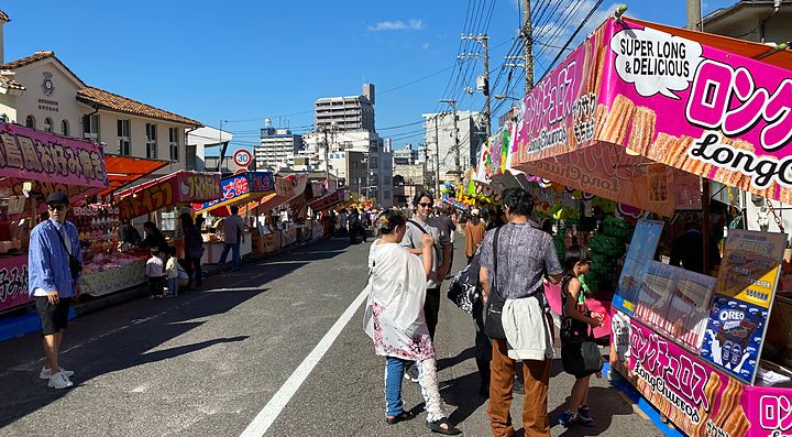 Bancarelle di cibo colorate lungo una strada di Hiroshima durante un festival locale con persone che camminano.