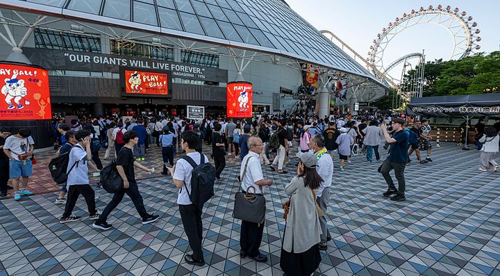 Persone camminano davanti alla struttura a cupola del Tokyo Dome in Giappone durante una giornata di sole.