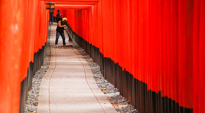 Una persona pulisce il sentiero tra i torii rossi di Fushimi Inari.