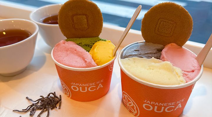 Due coppette di gelato con logo Ouca su un tavolo accanto a una vetrina che affaccia su una strada a Ebisu, Tokyo.